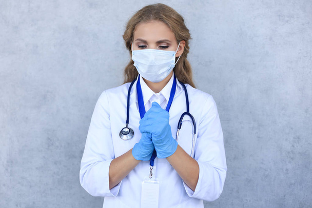 Donna medico in una maschera con gli occhi chiusi pregando isolato su sfondo grigio
. - Foto, immagini