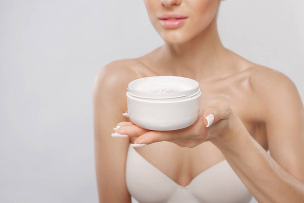 Skin care. Beauty Concept. Young woman holding cosmetic moisturizing cream. Soft skin and naked shoulders, model with light nude make-up, portrait of girl face with clean healthy skin. Dermatology - Fotoğraf, Görsel