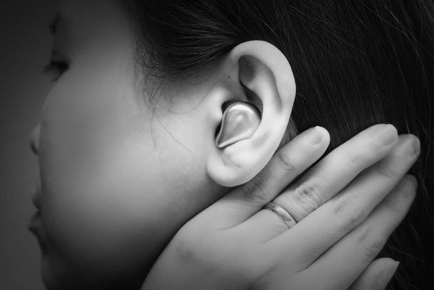 Настоящие беспроводные Bluetooth наушники в азиатской молодой женщины ухо, с пальцем, для комфортного общения или прослушивания музыки. Чёрно-белый тон
 - Фото, изображение