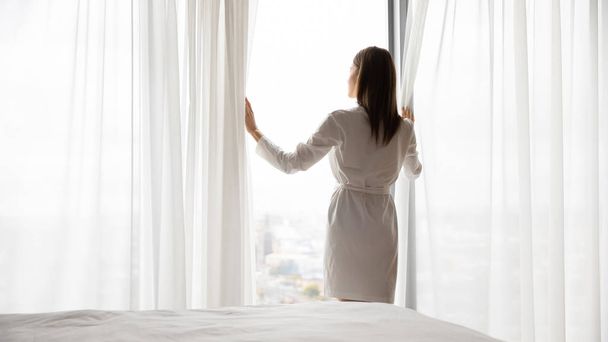Rückansicht schöne Frau schaut aus dem Fenster in moderne Wohnung - Foto, Bild