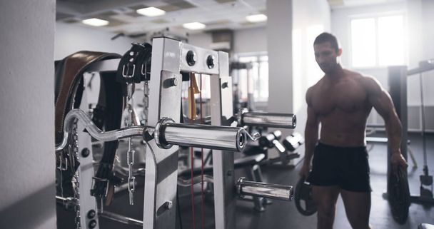 Portrait of muscular strong athletic man with naked torso pumping up muscles in the gym, brutal bodybuilder workout, sports nutrition and equipment concept - Φωτογραφία, εικόνα