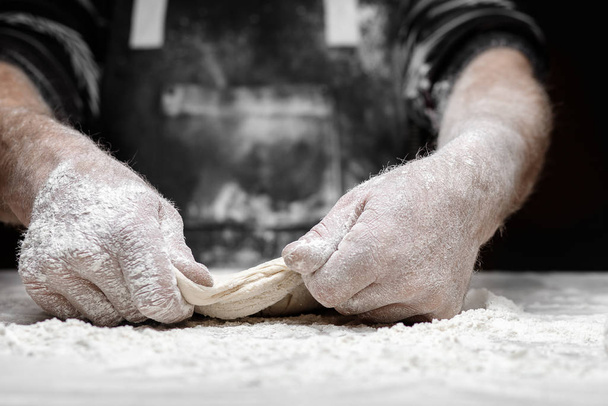 Bäckermeister streut Mehl frischen Teig auf Küchentisch, schwarzer Hintergrund - Foto, Bild