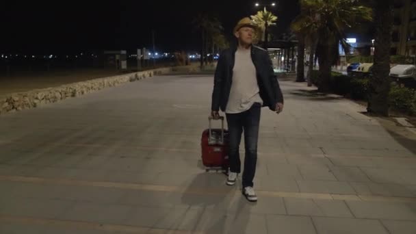 Utazó fickó kalapban és bőröndben sétált késő éjjel az utcán - Felvétel, videó