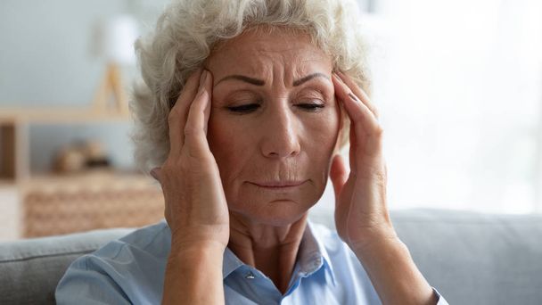 Закрыть несчастную пожилую женщину, трогающую виски, страдающую головной болью
 - Фото, изображение