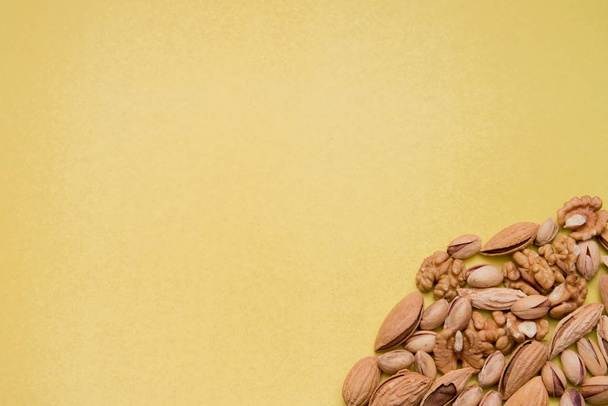 A variety of dried nuts lies on a yellow textured paper background. Peeled walnuts, pistachios and almonds. - Foto, Imagen