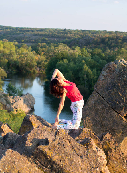 adult woman doing yoga asanas on the rocks above the river - 写真・画像