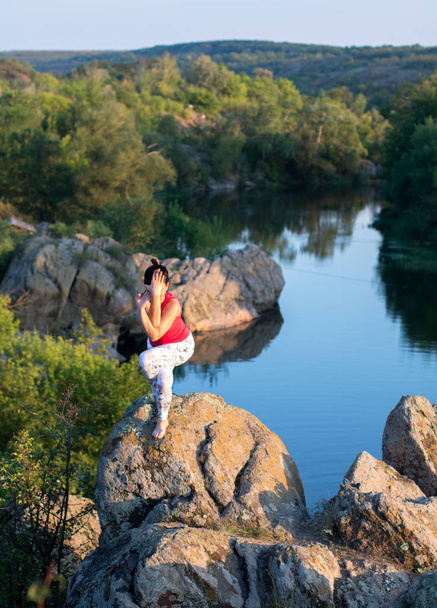 ενήλικη γυναίκα που κάνει yoga asanas στα βράχια πάνω από το ποτάμι - Φωτογραφία, εικόνα