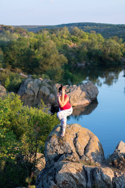 доросла жінка робить асан йоги на скелях над річкою
 - Фото, зображення