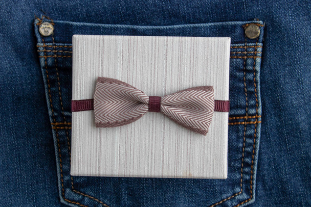 Невеличкий подарунок у ремісничому папері та коричневій стрічці в кишені блакитних джинсів. Зміст свят
 - Фото, зображення