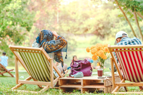 Счастье пара на летний отдых сидя на садовых стульях, чтобы расслабиться в общественном парке. - Фото, изображение