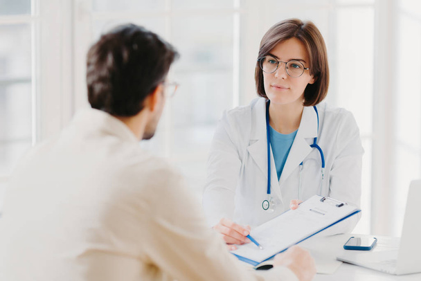 Female general practitioner explains which prescribed medicine patient should buy, gives medical visit consultation. Male clinic visitor tells about health complaints to therapist. Healthcare concept - Photo, Image