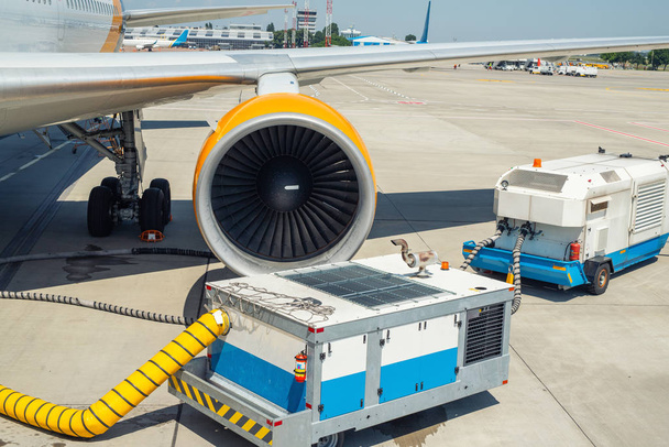 Egy nagy, modern kereskedelmi repülőgép parkol a repülőtéri kifutópályán, és csatlakozik a földi energiaellátó egységhez. A légi jármű karbantartása és ellenőrzése repülés előtt. Repülőtéri kiszolgálás - Fotó, kép