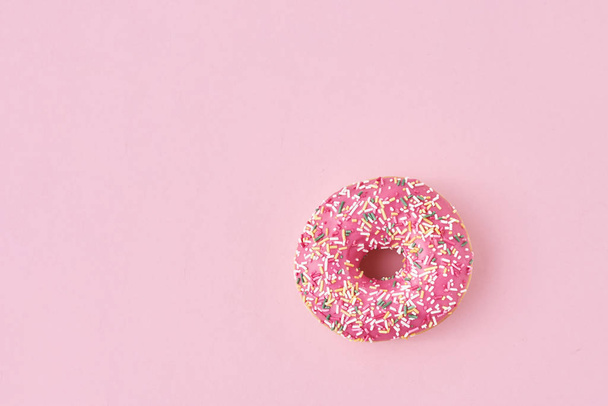 donats decorated sprinkles and icing on a pink background. Creative and minimalis food concept, top view flat lay - 写真・画像