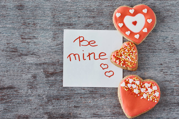 Cookies en forme de cœur déoculé et feuille de papier avec inscription être le mien sur le fond gris. Concept Saint-Valentin
 - Photo, image