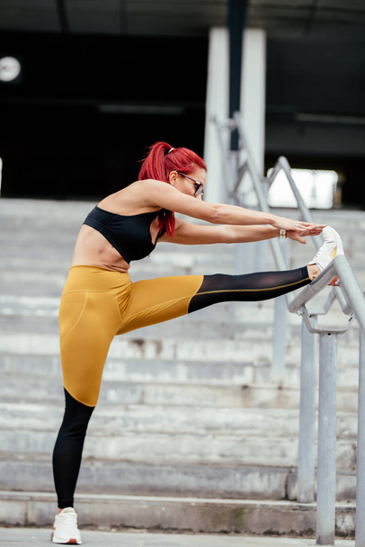 Fitness young woman stretching outdoors and doing warm up exercises. Training and working out sportswoman concept. - Foto, Imagem
