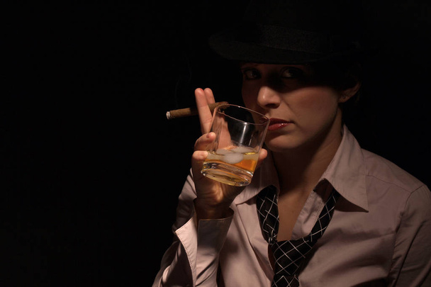 young woman in a black hat and glasses with a glass of whiskey - Foto, imagen