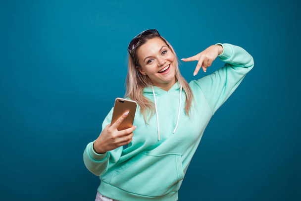 Stylish trendy hipster girl in the blue hoodie with the hood uses a smartphone. - Fotó, kép