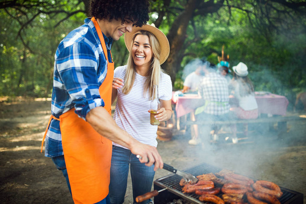 Young couple preparing sausages on a grill outdoors - Foto, afbeelding