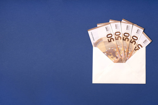 Euro-Schein im Umschlag. Euro-Scheine auf blauem Hintergrund. Geldsparen, Geschenk, Lieferkonzept für Bargeld. .. - Foto, Bild