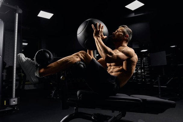 Man building core nuscles with ball on bench. - 写真・画像