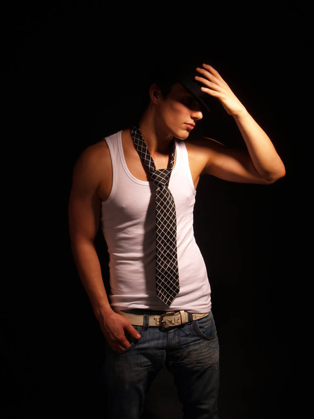 young handsome man in black shirt and jeans posing on dark background - Photo, Image