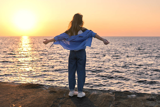 Happy Teenage girl standing with her hands outstretched on a sea pier at sunset - Fotó, kép