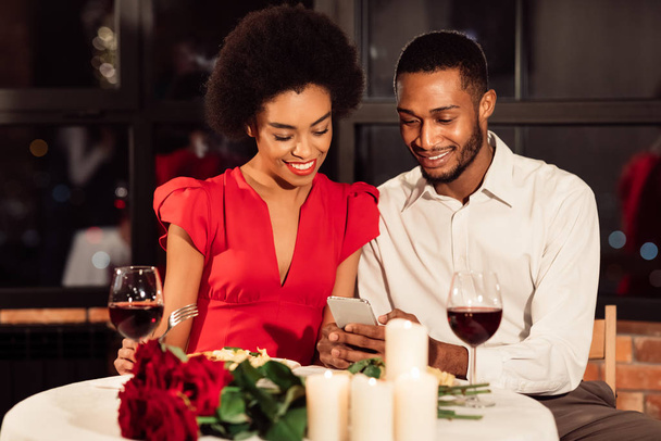Cónyuges afroamericanos usando el teléfono celular durante la cita en un restaurante elegante
 - Foto, imagen