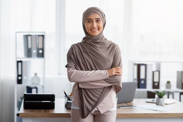 Empresaria musulmana de confianza de pie con los brazos cruzados cerca del lugar de trabajo en la oficina
 - Foto, imagen