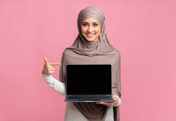 Feliz chica musulmana sosteniendo portátil con pantalla negra en la mano
 - Foto, imagen