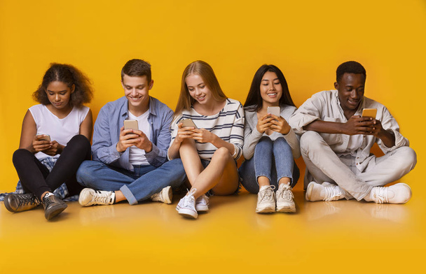 Nastolatki siedzą na podłodze i smsują smartfonami - Zdjęcie, obraz