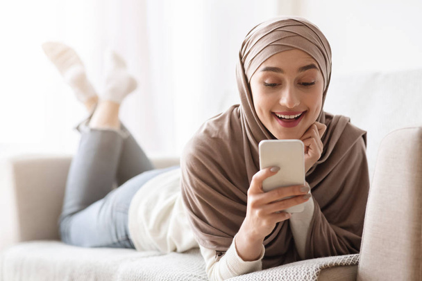 Gelukkig moslim meisje in hijab kijken naar smartphone scherm met opwinding - Foto, afbeelding