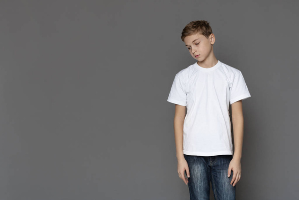 Sad teen boy standing alone, grey studio background - Photo, Image
