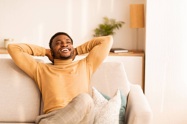 glücklich Afro-Mann entspannt sitzen auf Sofa drinnen, Kopierraum - Foto, Bild
