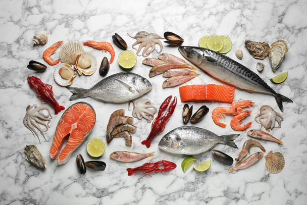 frischer Fisch und verschiedene Meeresfrüchte auf weißem Marmortisch, flach gelegt - Foto, Bild