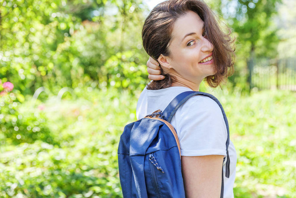 Heureuse étudiante positive avec sac à dos souriant sur fond de parc vert
 - Photo, image