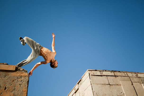 Young man jumping and practicing parkour between two building outside on clear summer day - Foto, Imagen