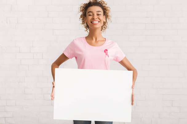 Bénévolat en T-shirt rose tenant une affiche vierge debout à l'intérieur, maquette
 - Photo, image