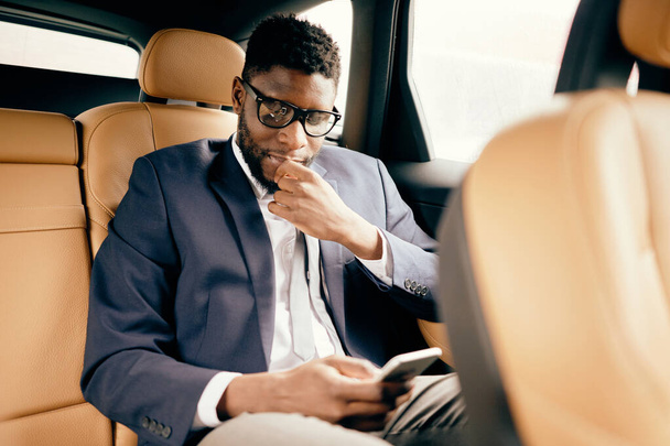 Businessman in a suit sits in a car back seat using his phone. - Foto, Bild