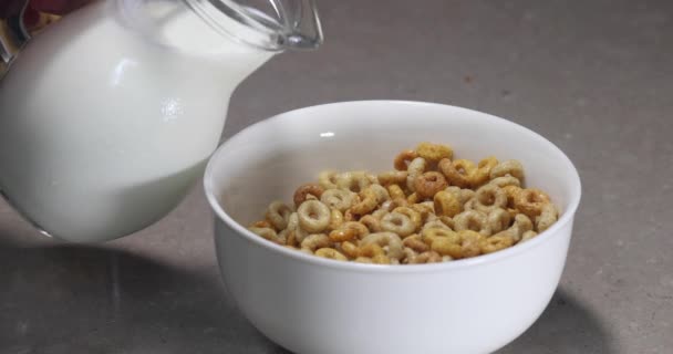 Gezond ontbijt. Een vrouw giet melk in een kom met cornflakes uit een glazen kan. - Video
