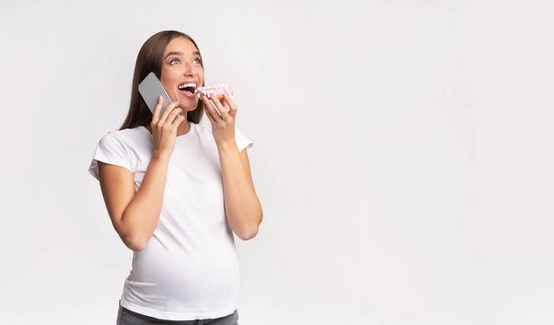 Zwangere dame eten Donut chatten op mobiele telefoon, Studio schot - Foto, afbeelding