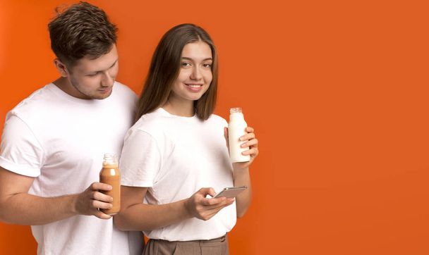 Young couple drinking detox smoothies, girl using cellphone - Φωτογραφία, εικόνα