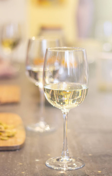 Refreshing white wine in glasses standing side by side on a table with candle in the sun light, blurred background. - Photo, image