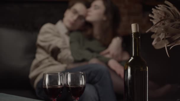 Bottle of wine and glasses and couple hugging on background, focus transition - Filmati, video