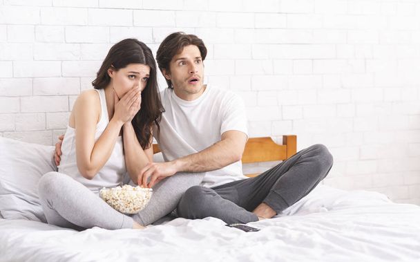 Amazed and scared couple watching scary movie on bedroom - Фото, изображение