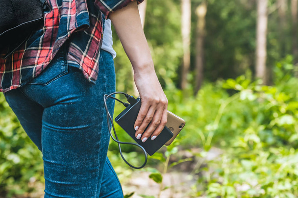 Power bank in a girl s hand, against the background of the forest and greenery. - Foto, afbeelding