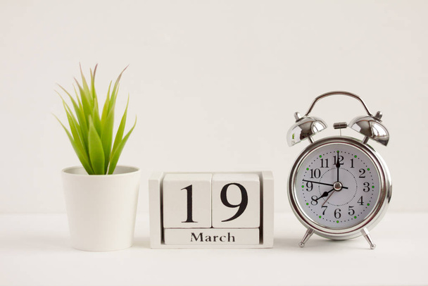 March 19 on a wooden calendar next to an alarm clock and a flower on a white background. The concept of one day a year.Significant date or event - Foto, Bild