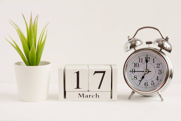 17. März auf einem hölzernen Kalender neben einem Wecker und einer Blume auf weißem Hintergrund. das Konzept eines Tages im Jahr. Bedeutsames Datum oder Ereignis - Foto, Bild