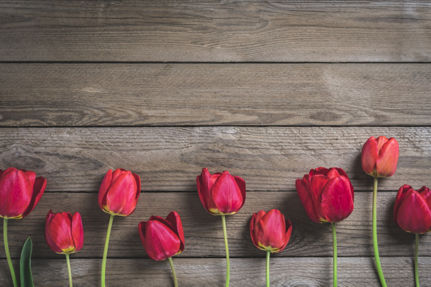 Riga di tulipani rossi su sfondo di legno con spazio per testo, messaggio. Festa della mamma, Ciao concetto di primavera. Il card. Piatto. Vista dall'alto. Stile rustico. Tonica
.  - Foto, immagini