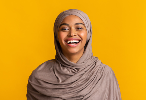 Портрет искренне смеющейся черной мусульманки на жёлтом фоне
 - Фото, изображение
