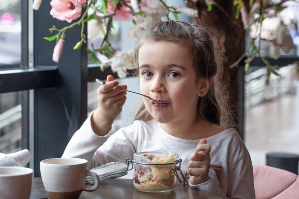 Gyönyörű kislány desszertet eszik egy kávézóban.. - Fotó, kép